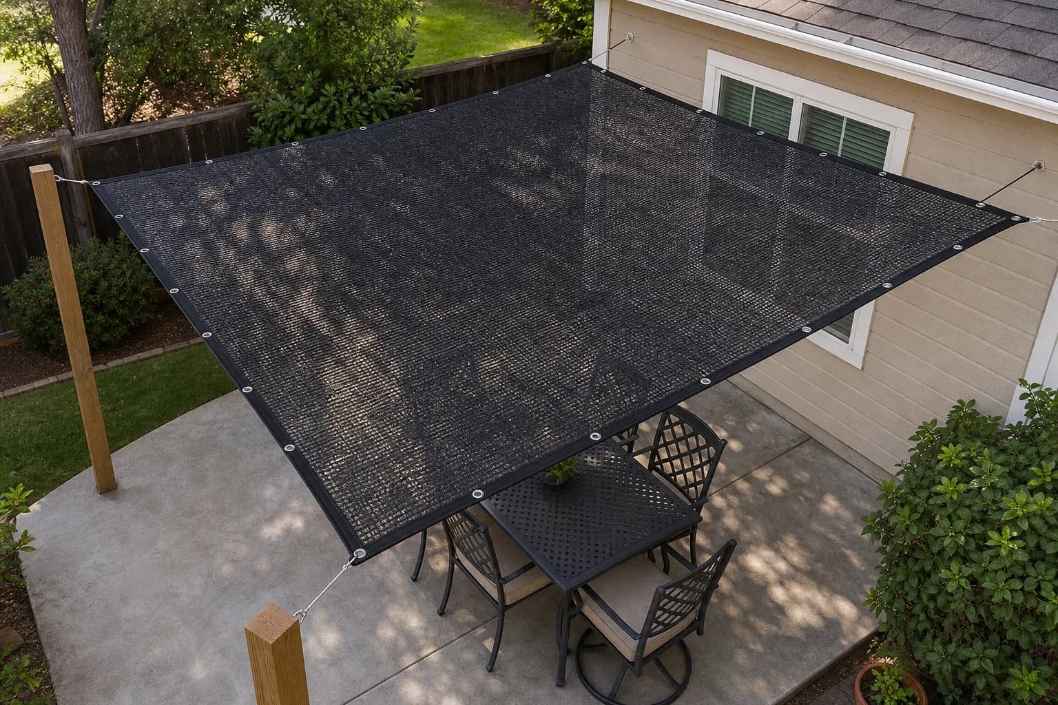 Rectangular black HDPE knitted shade cloth with a reinforced stitched perimeter and metal grommets, tied over a patio